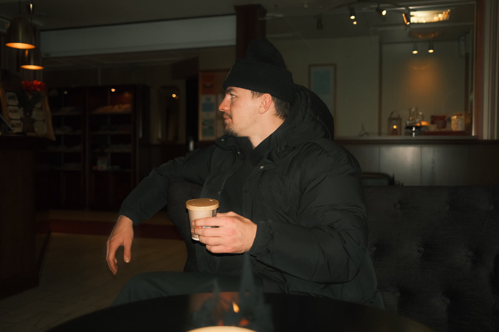 Pelle sitting alone with a coffee in a dim hotel lobby, looking away from the room