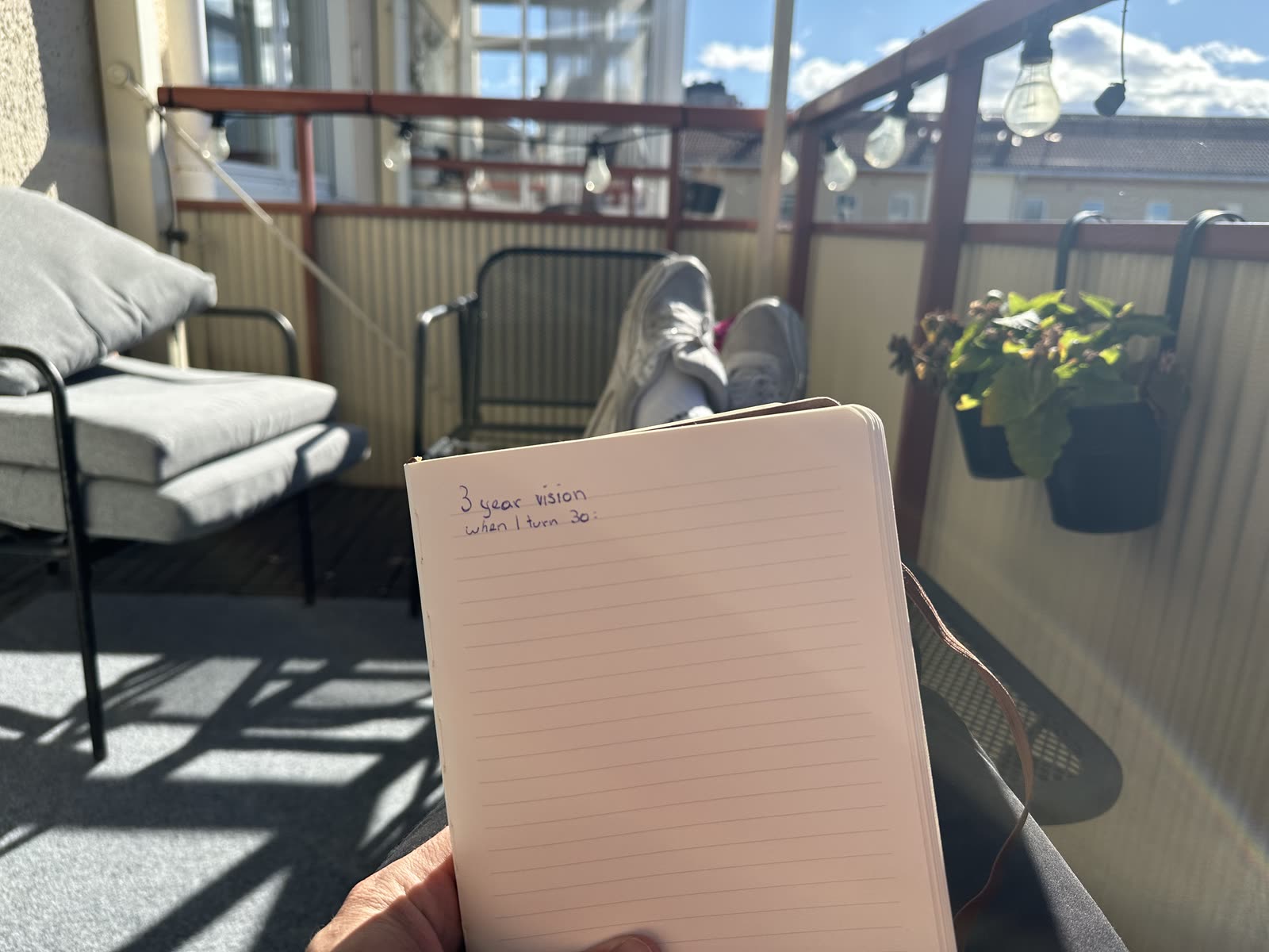 An open notebook on a sunlit balcony, headed "3 year vision, when I turn 30" above a blank page