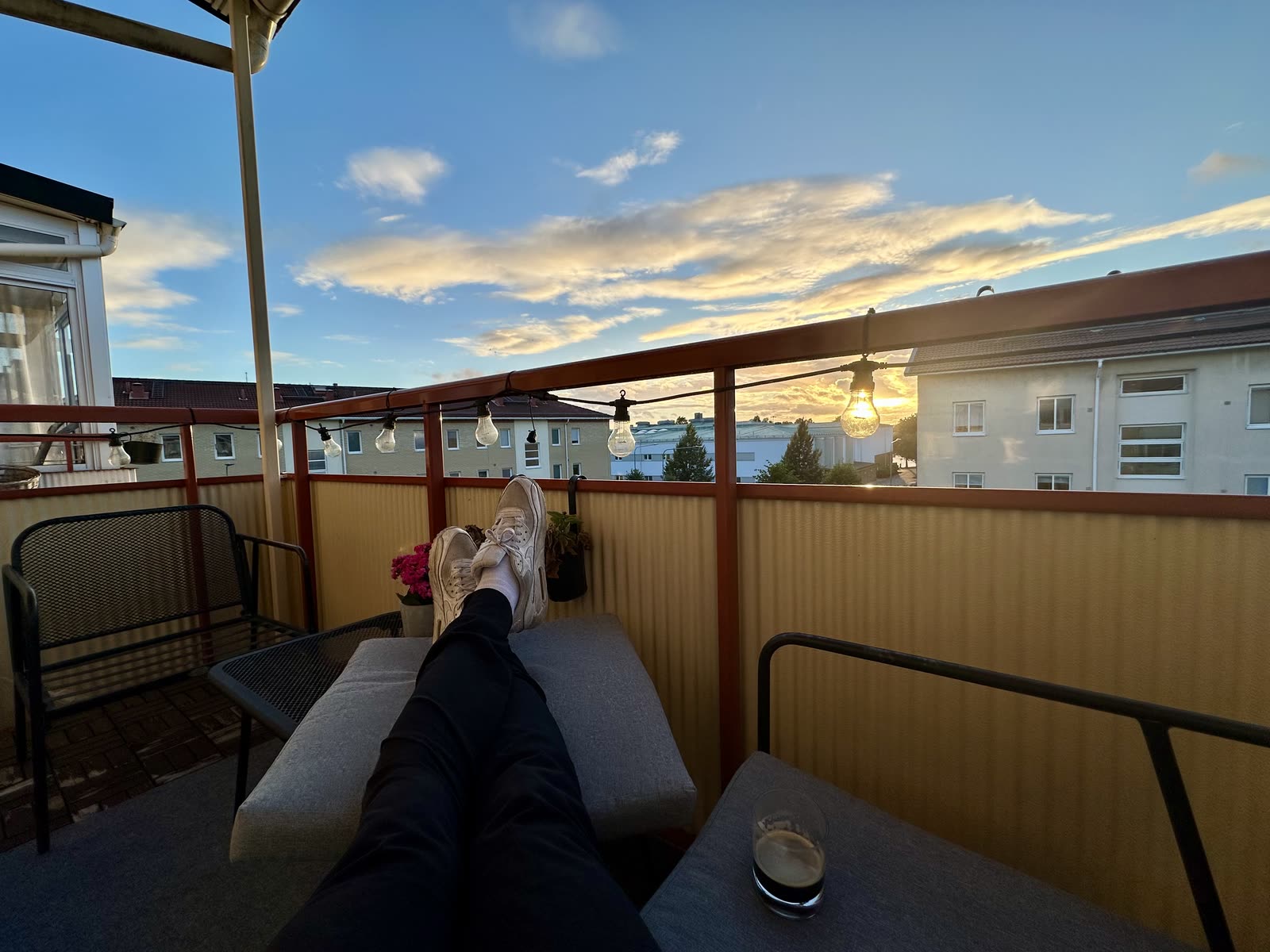 Pelle's legs stretched out on a balcony sofa at sunset, string lights and rooftops beyond the railing